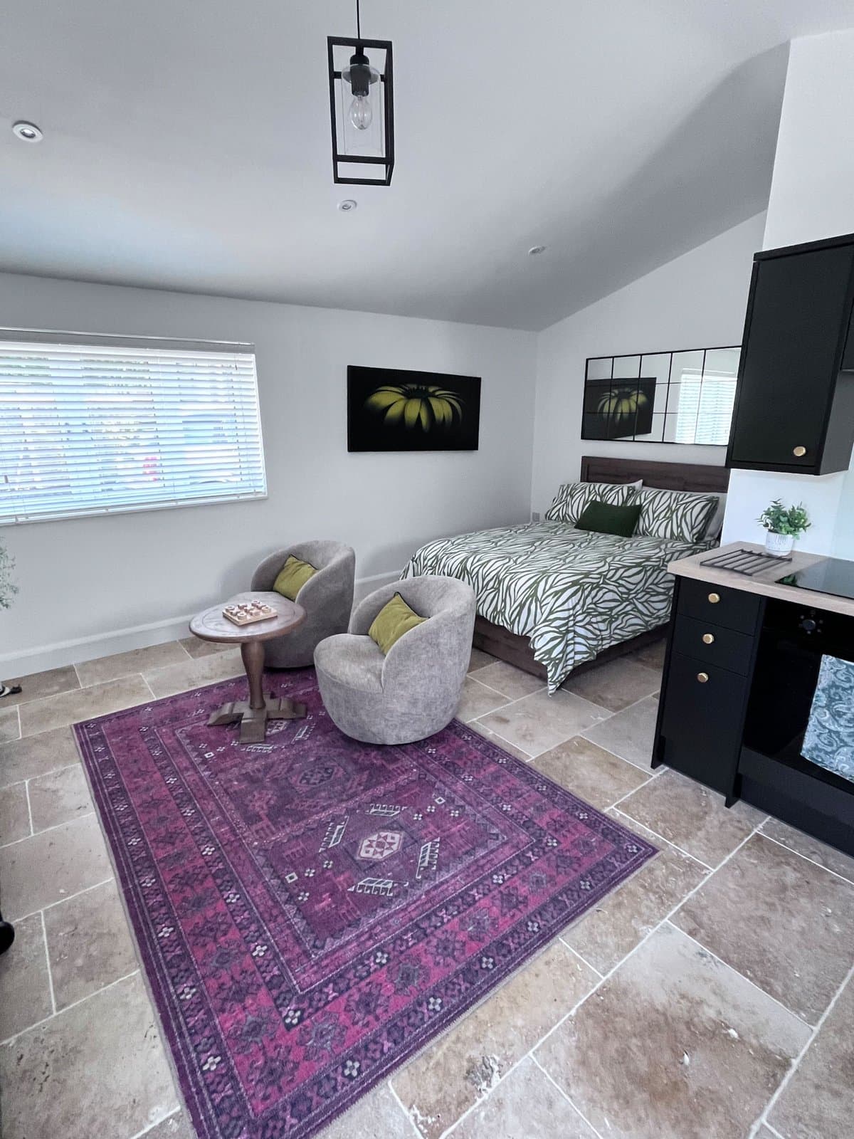 The studio from the doorway, with the bed, the sitting area and a purple rug on stone floors